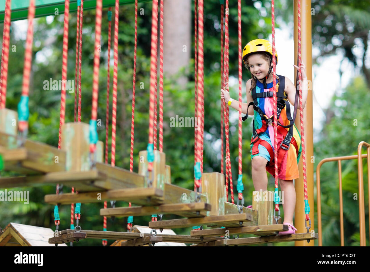 Child in forest adventure park. Kids climb on high rope trail. Agility