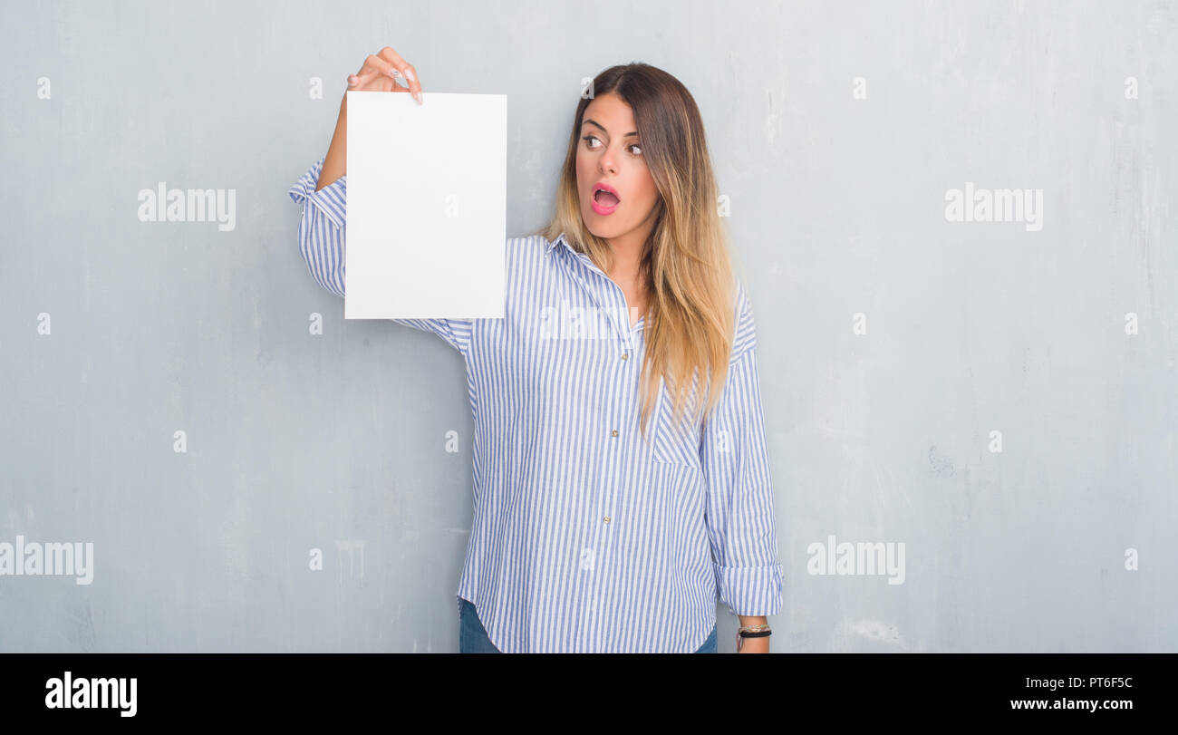 Afraid Paper Young adult woman over grey grunge wall holding blank paper sheet ...