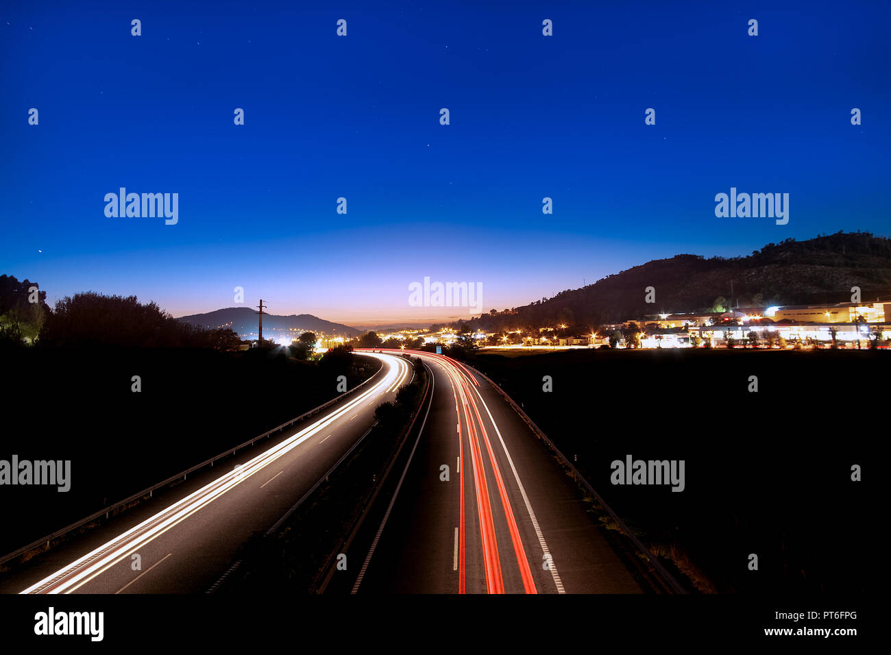 Long exposure night photography over the highway from Porto to city of Braga in Portugal. Fast car Light tracks and city lights at the dusk skyline. Stock Photo