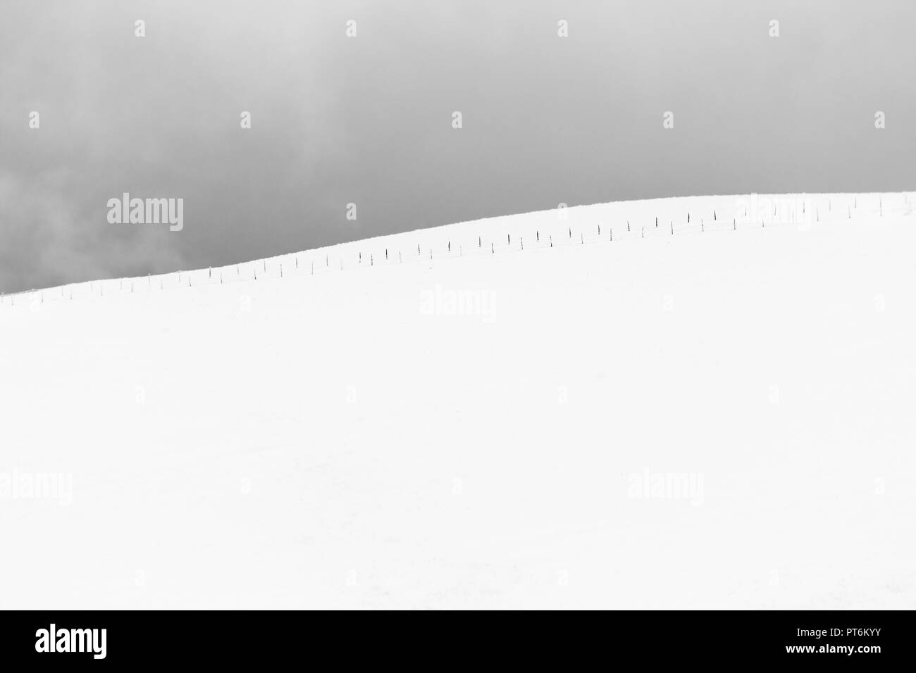 A very minimalistic view of a mountain covered by snow, with a fence Stock Photo