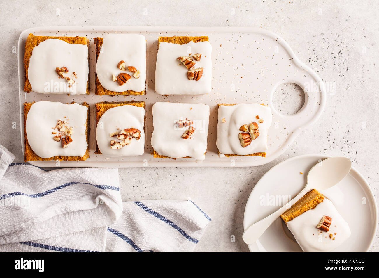 Vegan carrot cake with coconut cream and pecans on white board. Clean