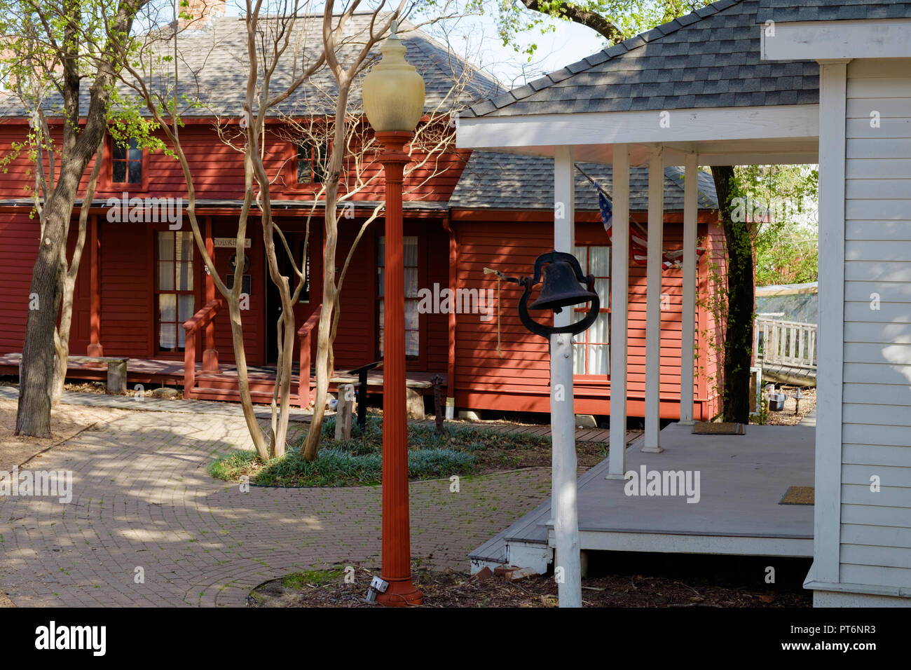 Red shingled house. White house on right, old school bell. Street lamp American flag on extended pole. Chestnut Square Historic Village,McKinney,Texas Stock Photo