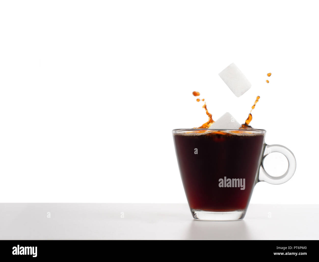 Sugar cubes falling into coffee with splash, health concept. Plain background for copyspace. Glass cup. Stock Photo