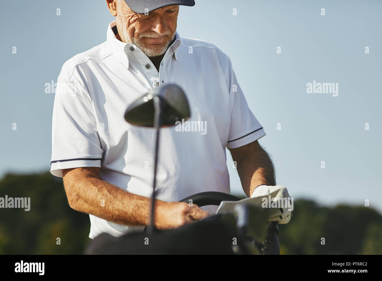 Sporty senior man reading his scorecard while enjoying a round of golf on a sunny day Stock Photo