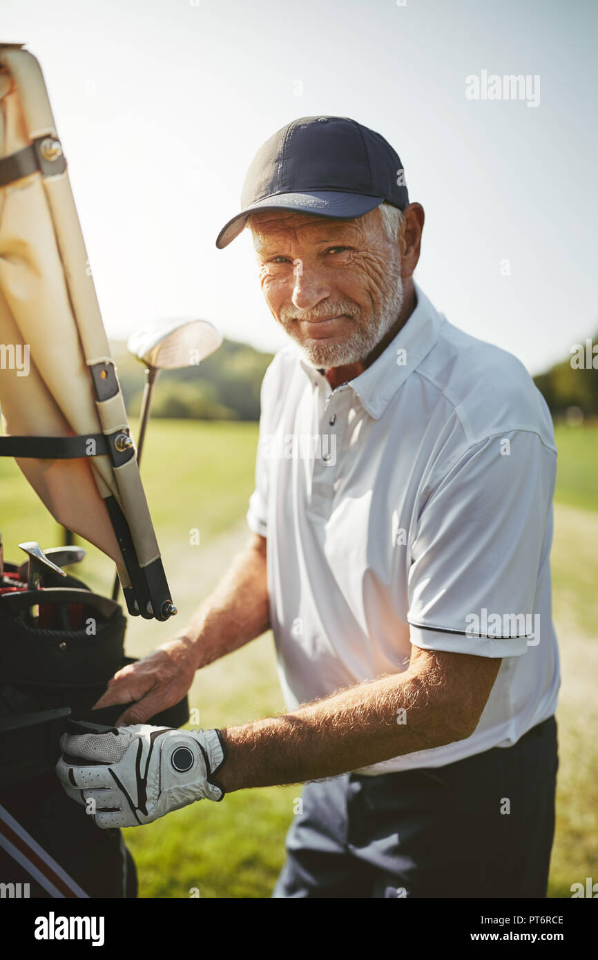 Smiling senior man putting his bag full of clubs on a cart while enjoying a round of golf on a sunny day Stock Photo