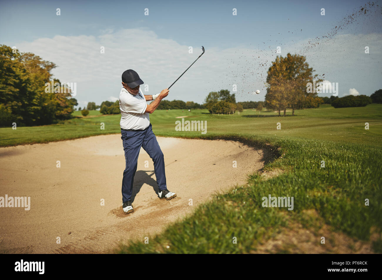 Senior man chipping out of a sand trap while playing a round of golf on a sunny afternoon Stock Photo