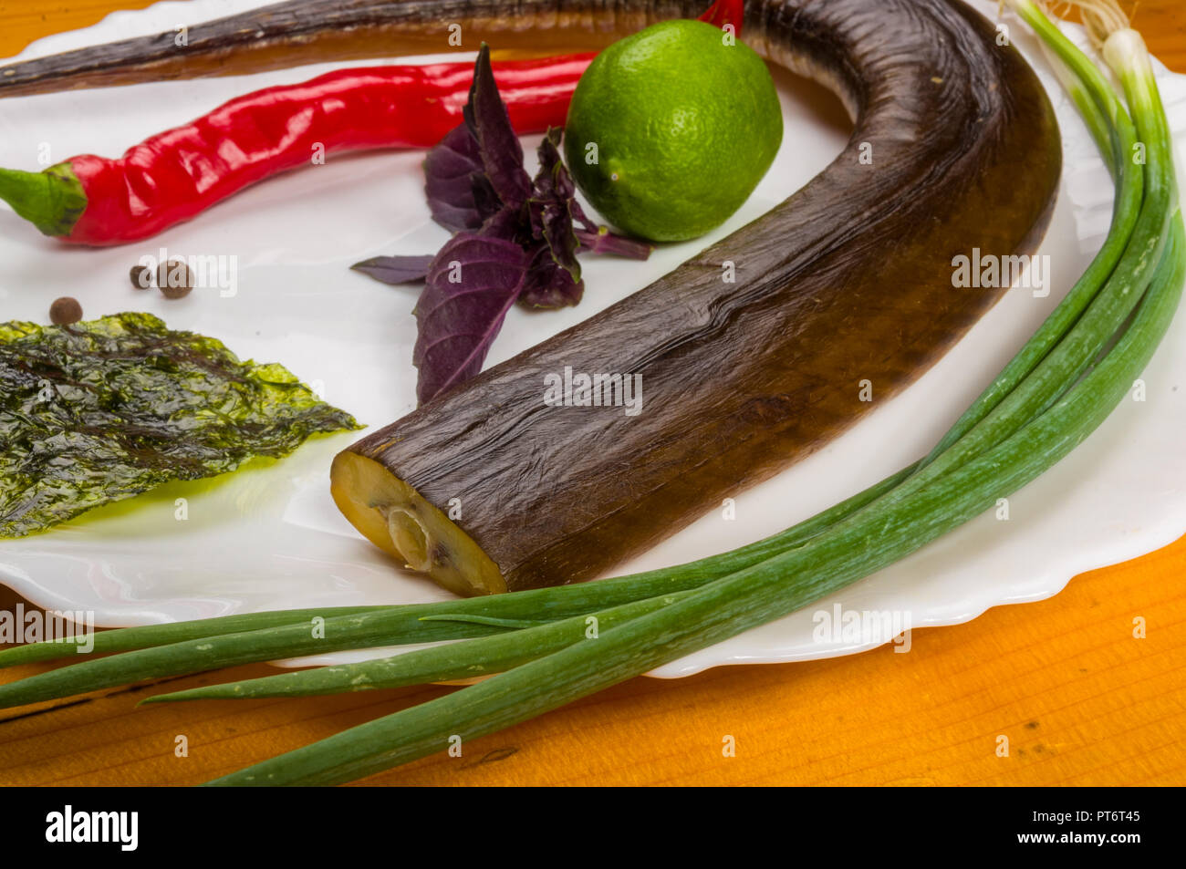 still life - smoked garfish with lime, Basil, green onions, chili, nori chips, spices, olive oil in a white ceramic dish, on a wooden table Stock Photo