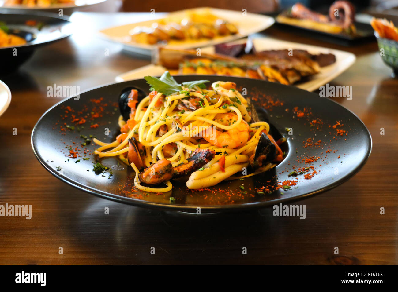 Healthy food concept. Spaghetti with shrimps, prawns, mussels and parsley on black plate. Blur plates with foods background. Stock Photo