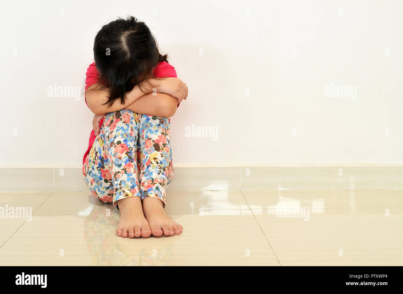 Sad little girl sitting on the floor Stock Photo - Alamy