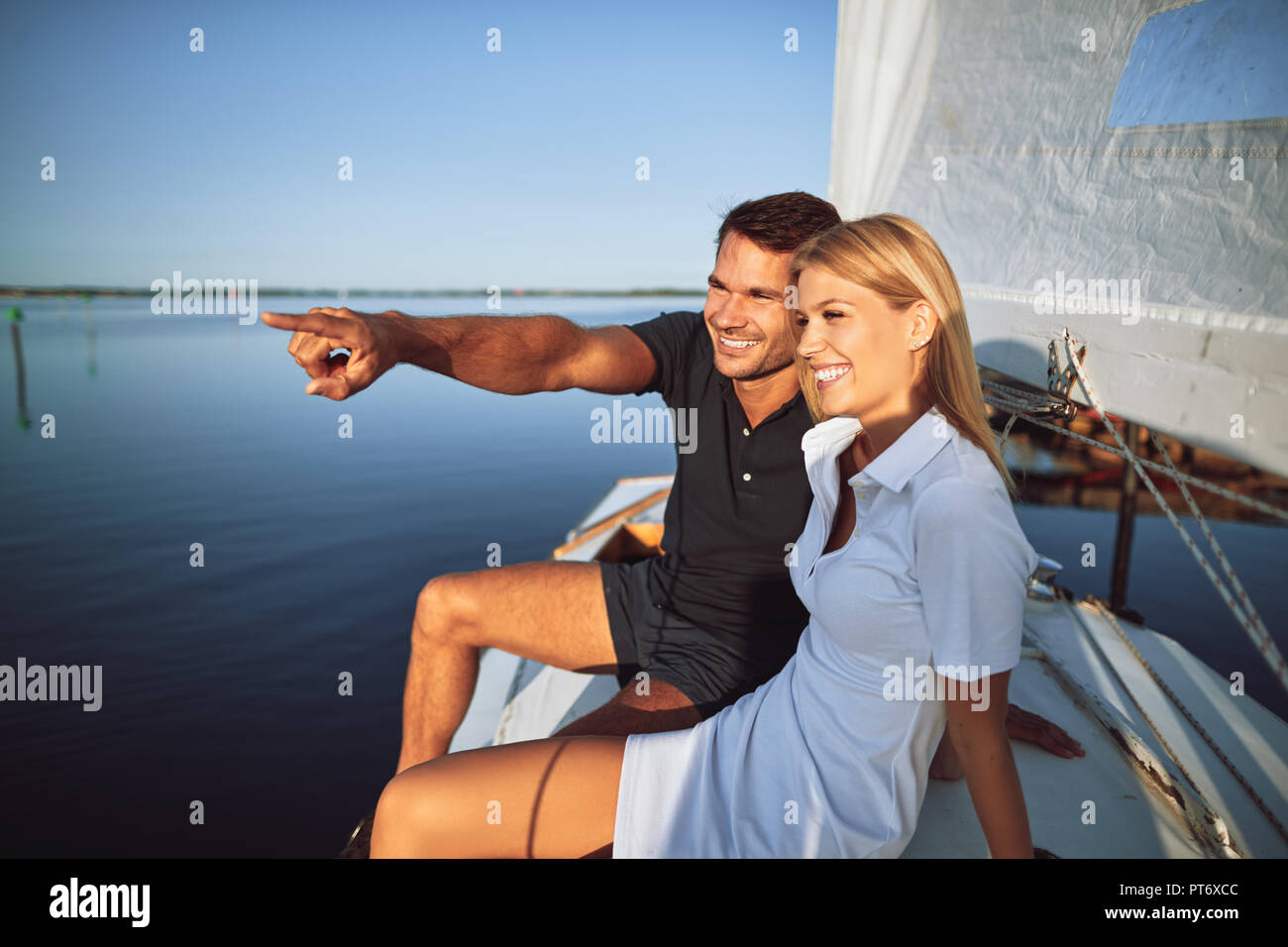 Young man pointing to something on the ocean horizon to his wife while sitting on the deck of their boat enjoying the day sailing Stock Photo
