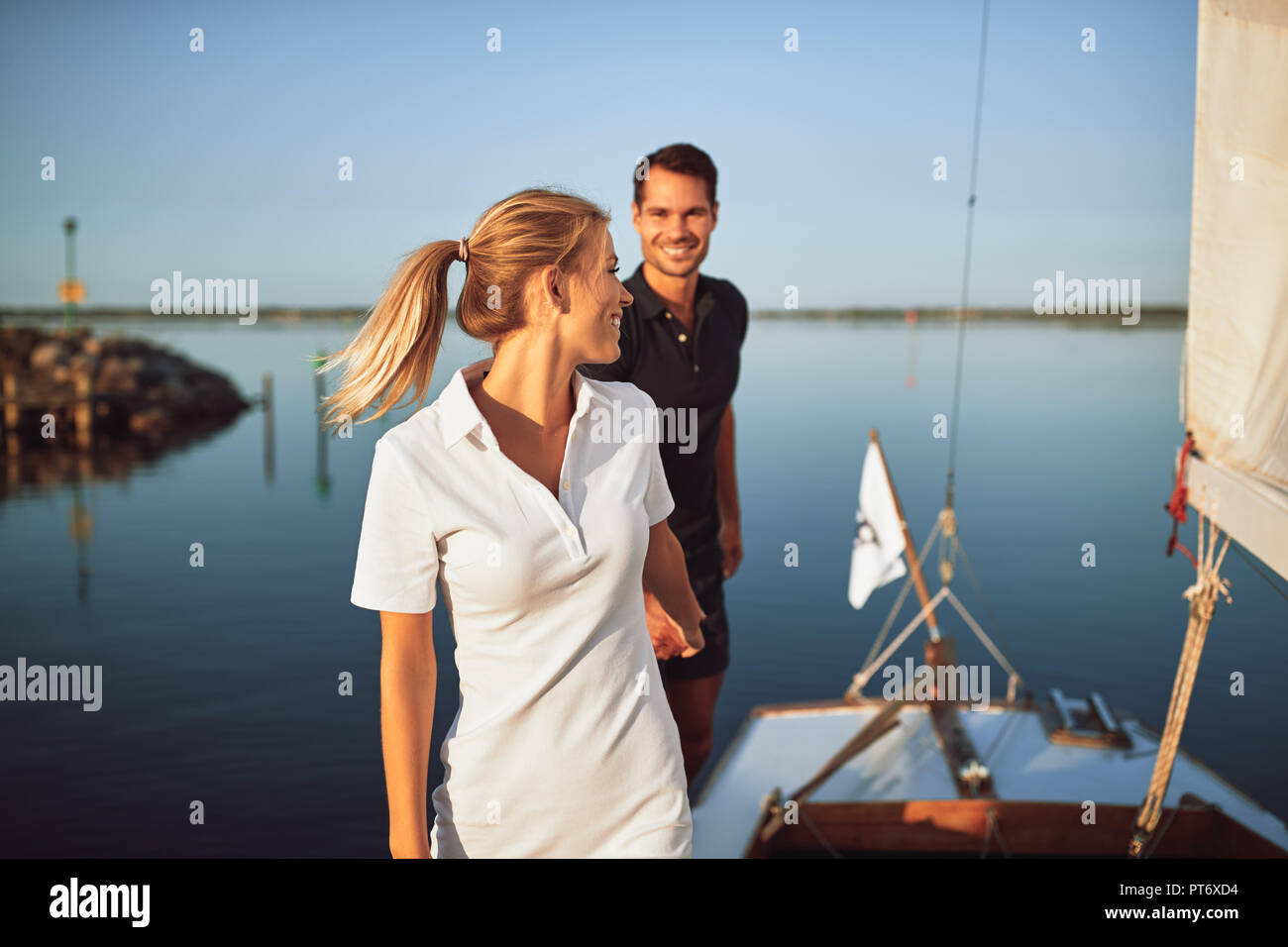 Young woman leading her husband by the hand on the deck of their yacht while enjoying a sunny day sailing together Stock Photo