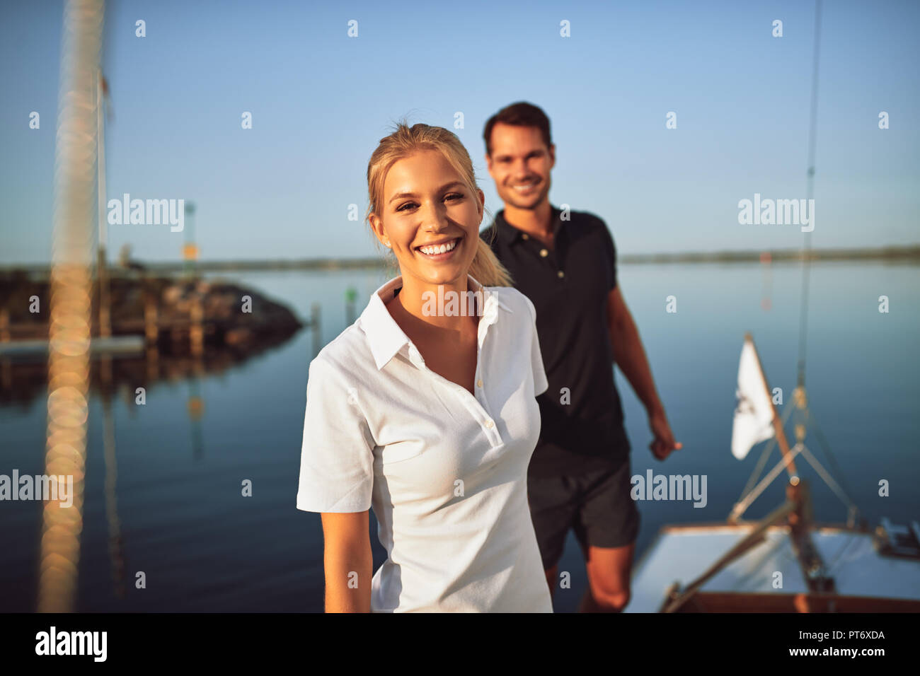 Smiling young woman standing on the deck of a yacht with her husband while enjoying the day sailing together Stock Photo
