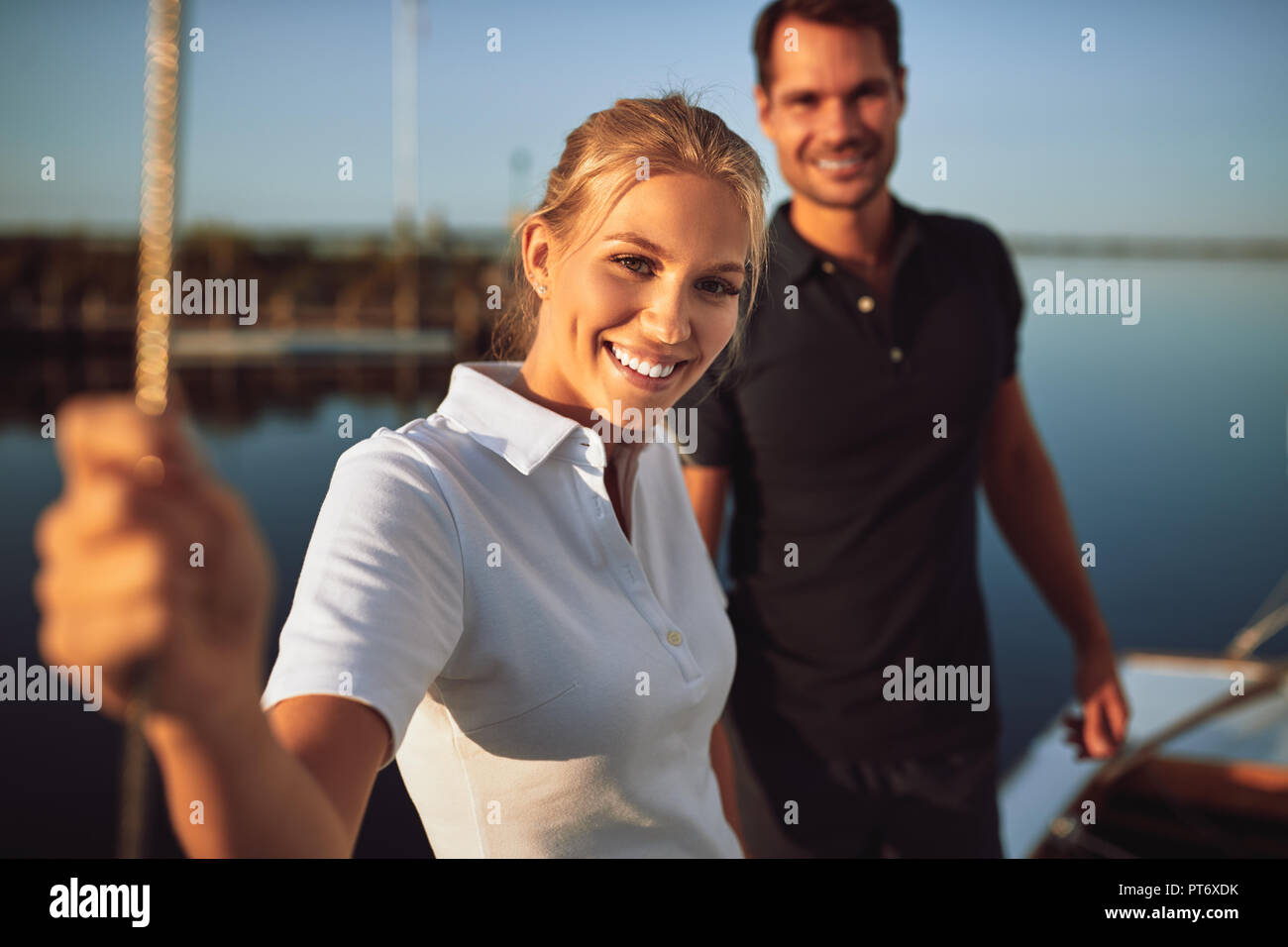 Smiling young husband and wife standing together on the deck of their yacht while enjoying a sunny day sailing Stock Photo