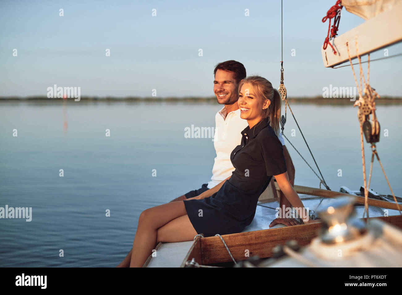 Smiling young couple enjoying the ocean view while sitting together on the deck of their boat on a sunny afternoon Stock Photo