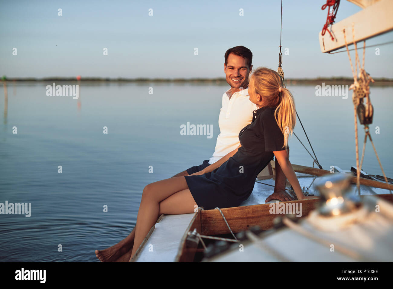 Smiling young husband and wife talking together while sitting on the deck of their boat enjoying an afternoon sailing Stock Photo