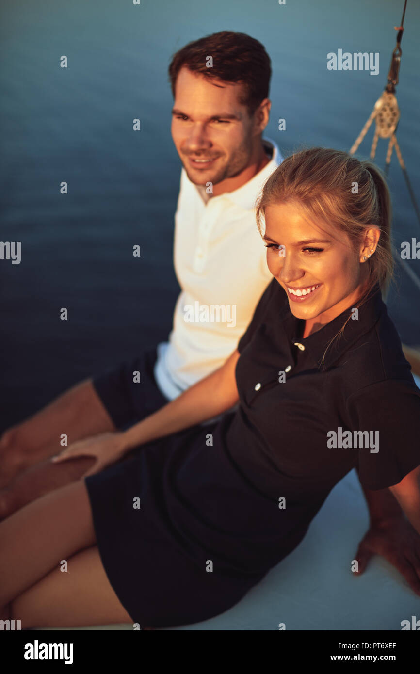 Smiling young couple enjoying the ocean view while sitting together on the deck of their sailing boat Stock Photo