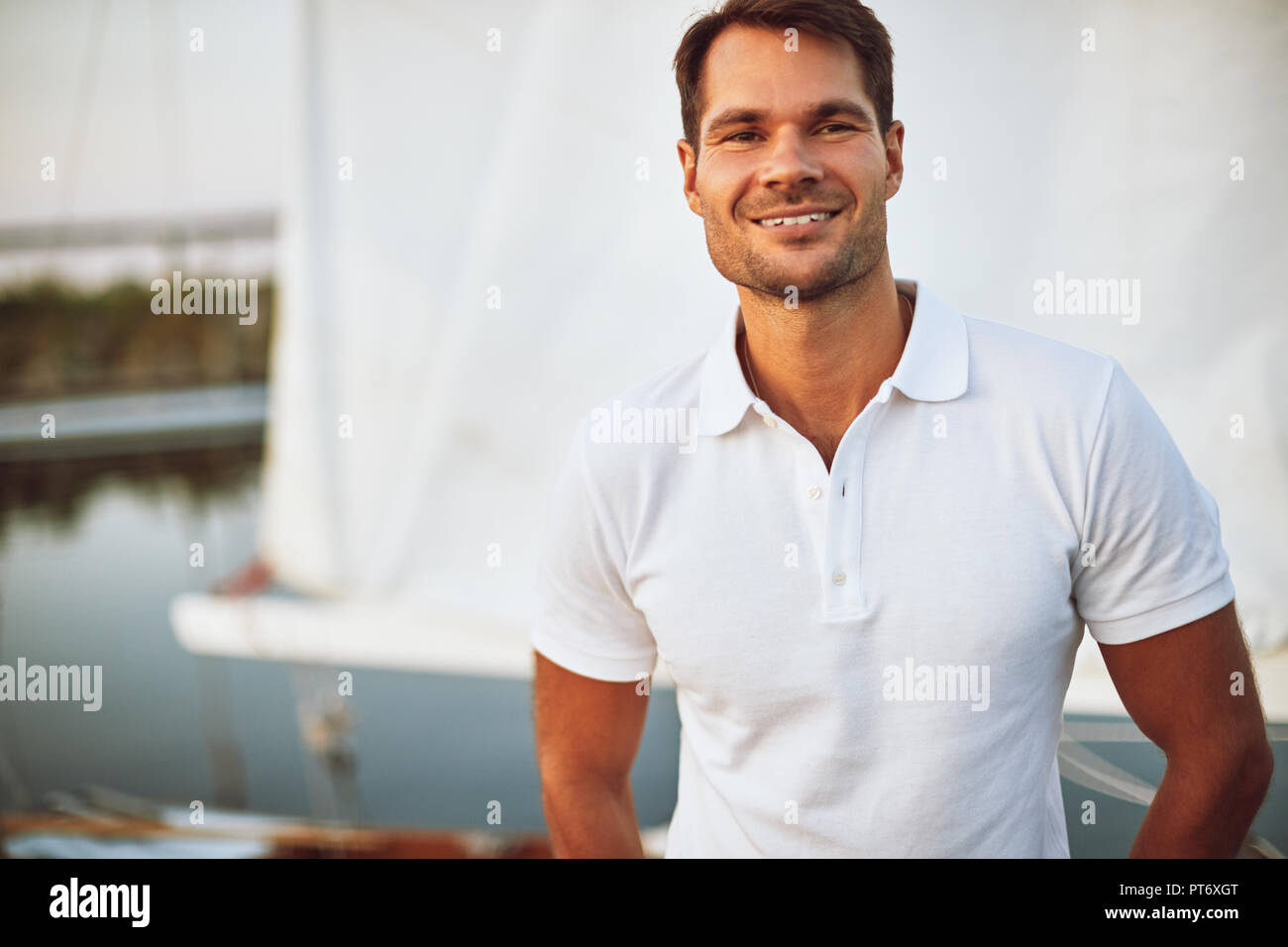 Smiling young man standing alone on the deck of his yacht enjoying a sunny day sailing Stock Photo