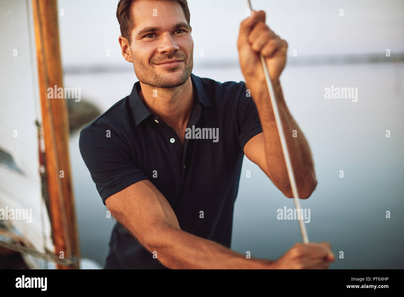 Handsome young man leaning on some rigging while standing on the deck of his yacht enjoying a sunny day sailing Stock Photo