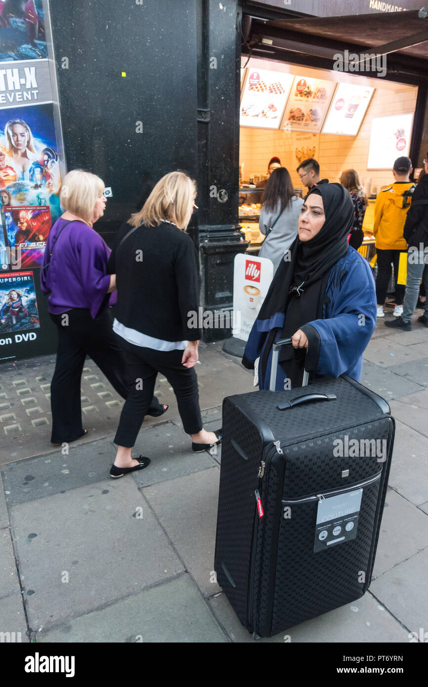 Muslim woman with very large wheeled suitcase on the street in london Stock Photo