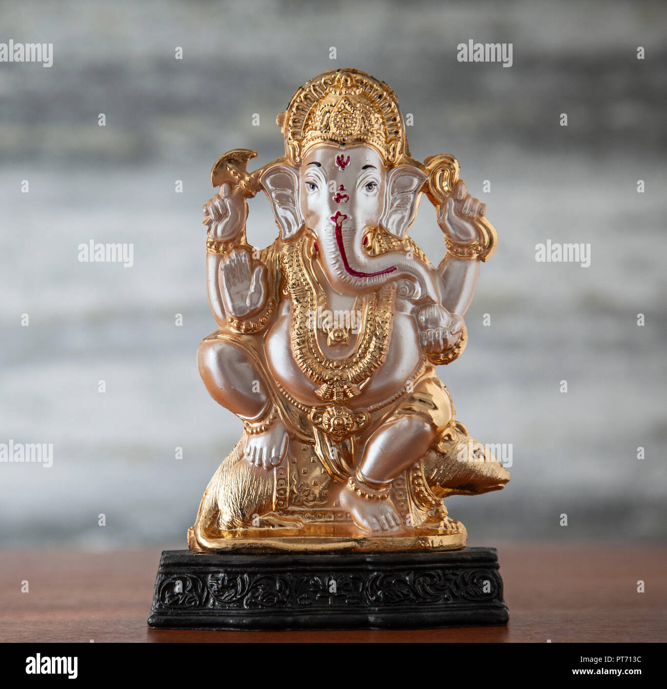 A small plastic murti of the Hindu deity Ganesh / Ganesha, sniffing a rice cake, riding a rat / mouse and holding an axe and noose. Stock Photo