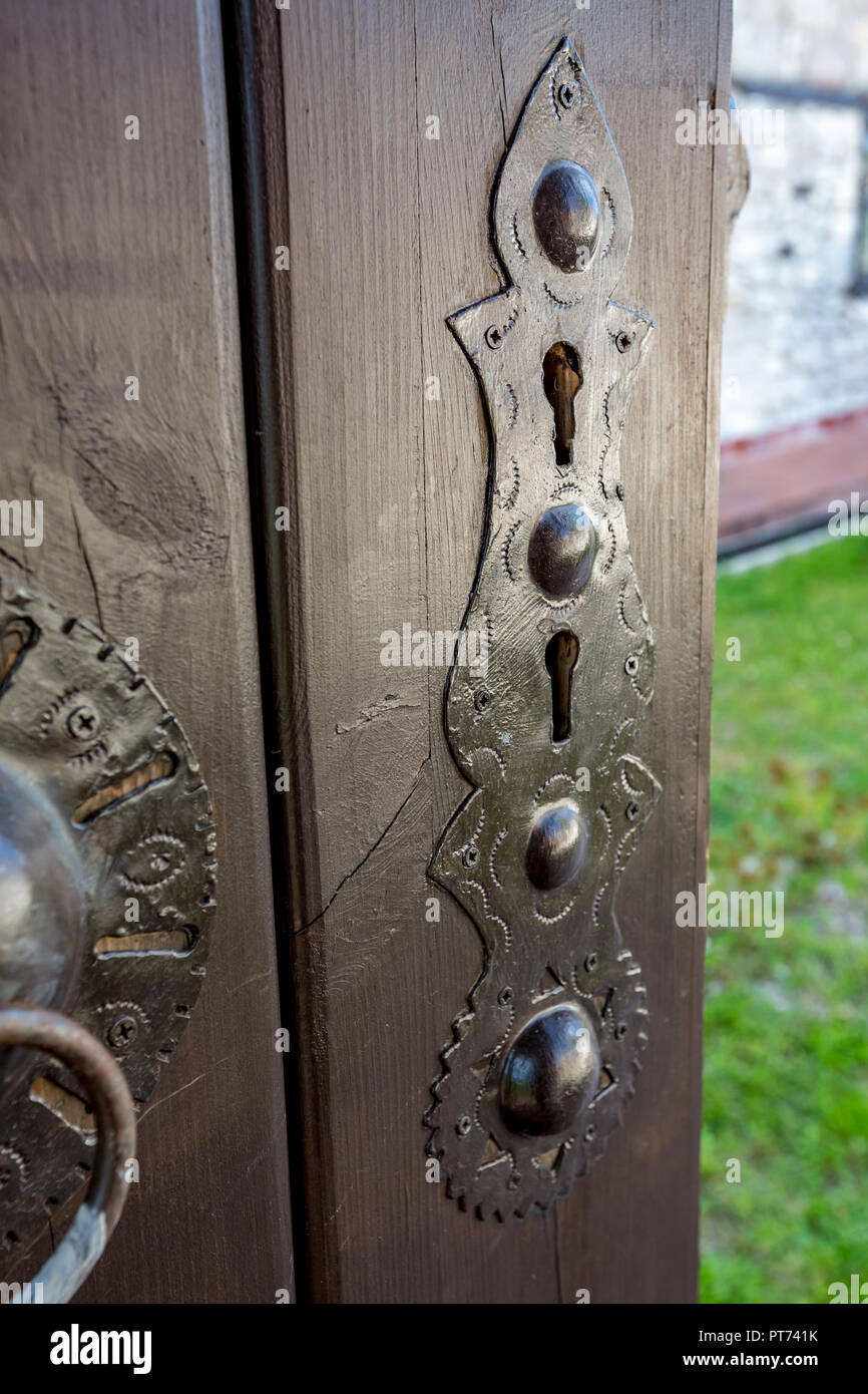 Wooden plank door with metallic double key hole escutcheon, brown painted, having nice ornamental decorations. Blurred springtime backyard. Bulgaria, village in Rhodope mountain Stock Photo