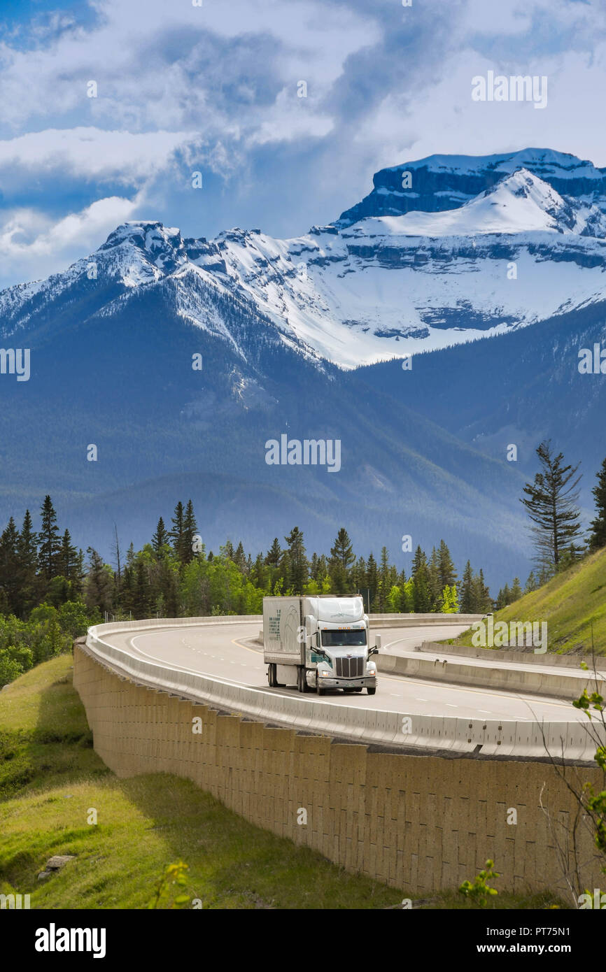 EN ROUTE REVELSTOKE TO LAKE LOUISE, AB - JUNE 2018: Large frieght truck passing snow capped mountains on the Trans Canada Highway approaching Lake Lou Stock Photo
