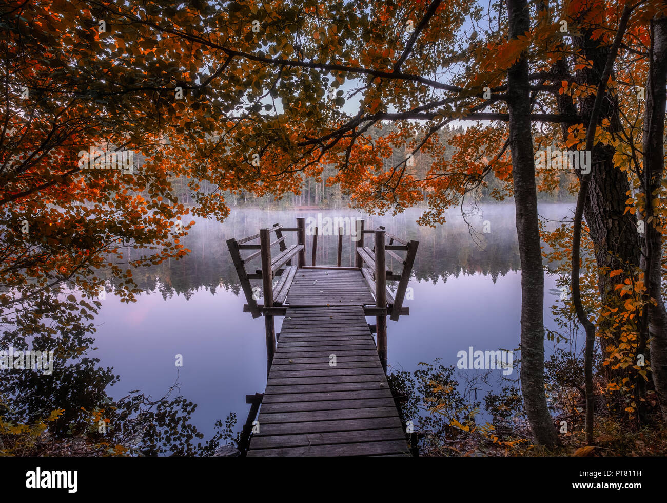 Beautiful fall colors with wooden pier and peaceful lake at autumn morning in Finland Stock Photo