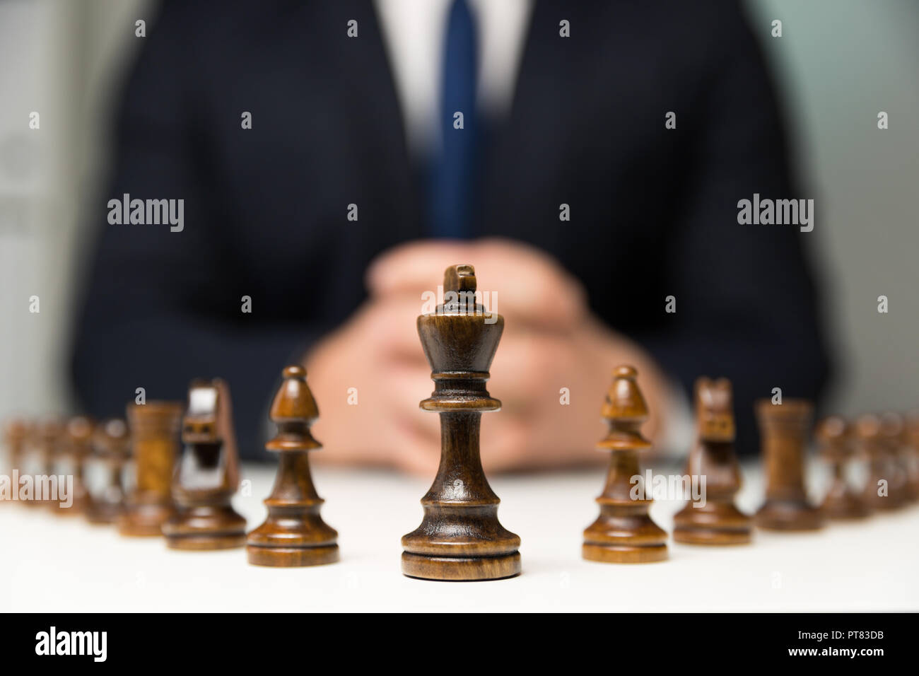Businessman with clasped hands planning strategy with chess figures on table. Strategy, leadership and teamwork concept. Stock Photo