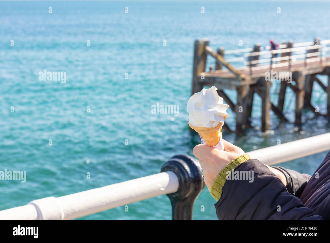 Womans Hands Holding an Ice Cream in a Cone With a Metal Rail and the Sea Beyond Stock Photo