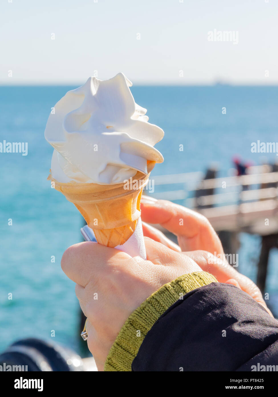 Womans Hands Holding an Ice Cream in a Cone With a Metal Rail and the Sea Beyond Stock Photo