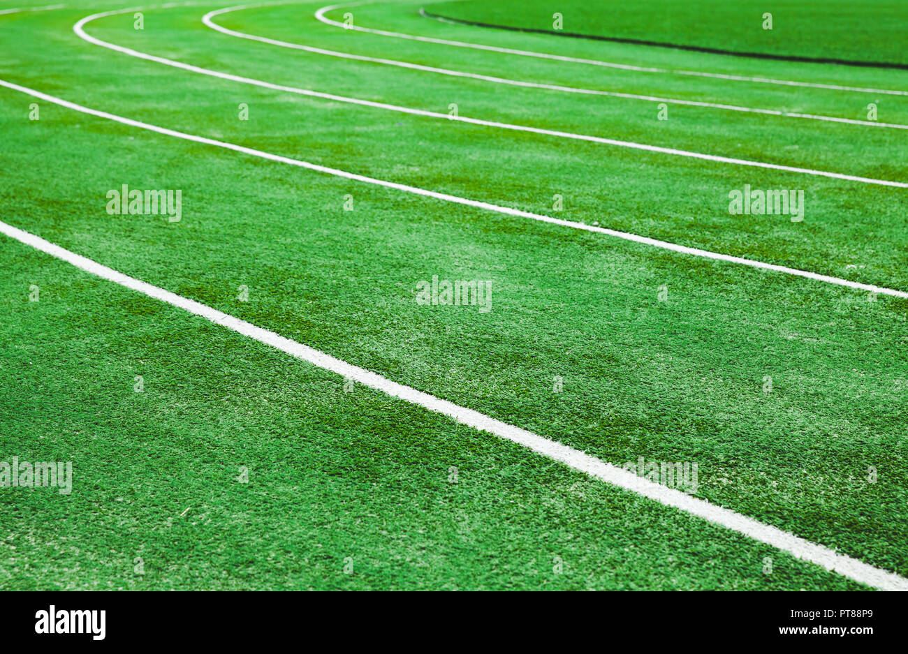 Empty running track with bright green artificial turf and lines Stock Photo