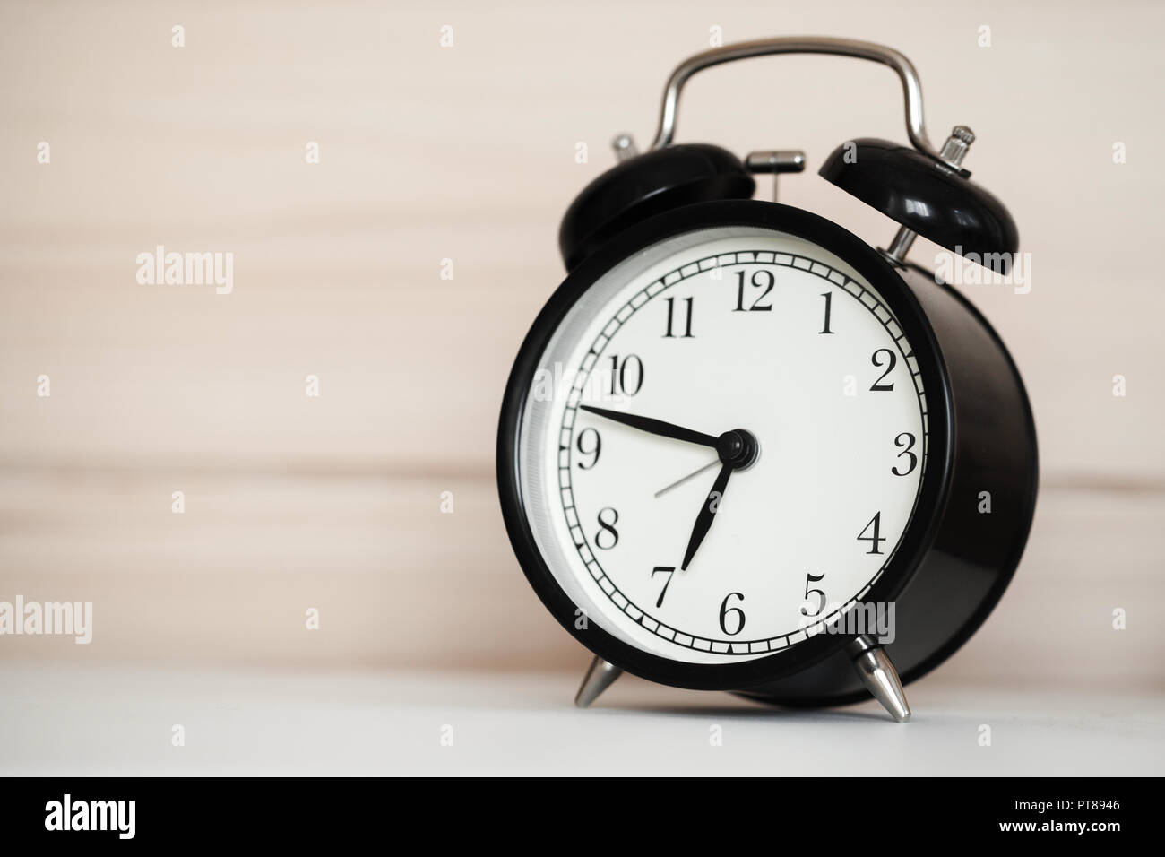 Vintage alarm clock is on a white bedside table near wooden wall Stock
