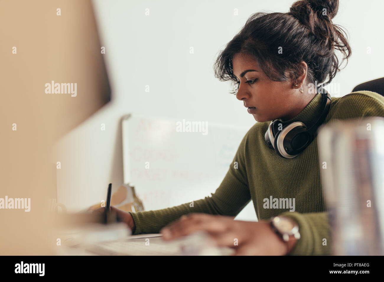 Woman making notes while working on computer. Female computer programmer working at her desk. Stock Photo