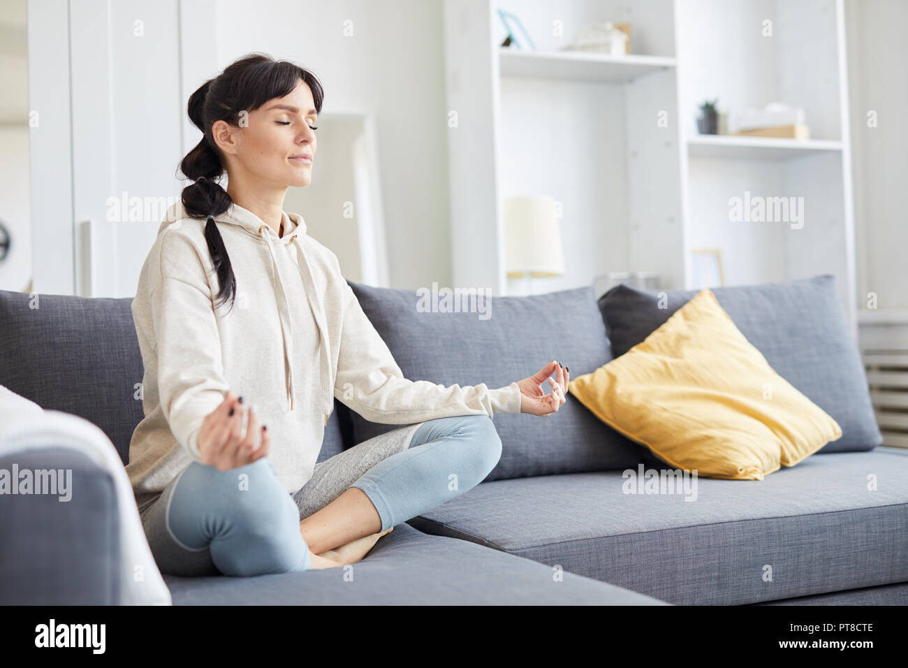 Young woman sitting in pose of lotus on sofa with her eyes closed during  yoga workout Stock Photo - Alamy