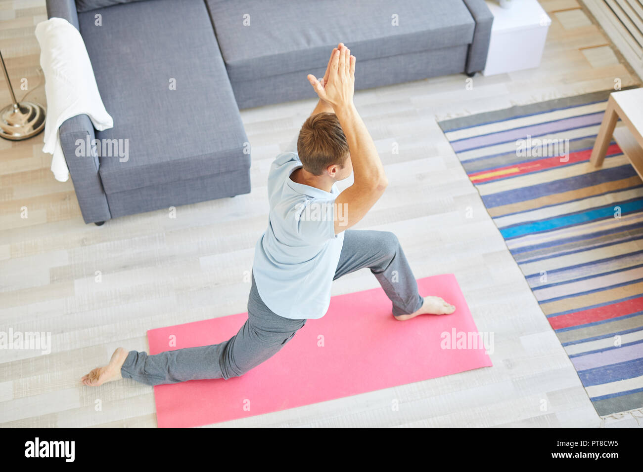 Active young man in shirt and sweatpants exercising on pink mat on the