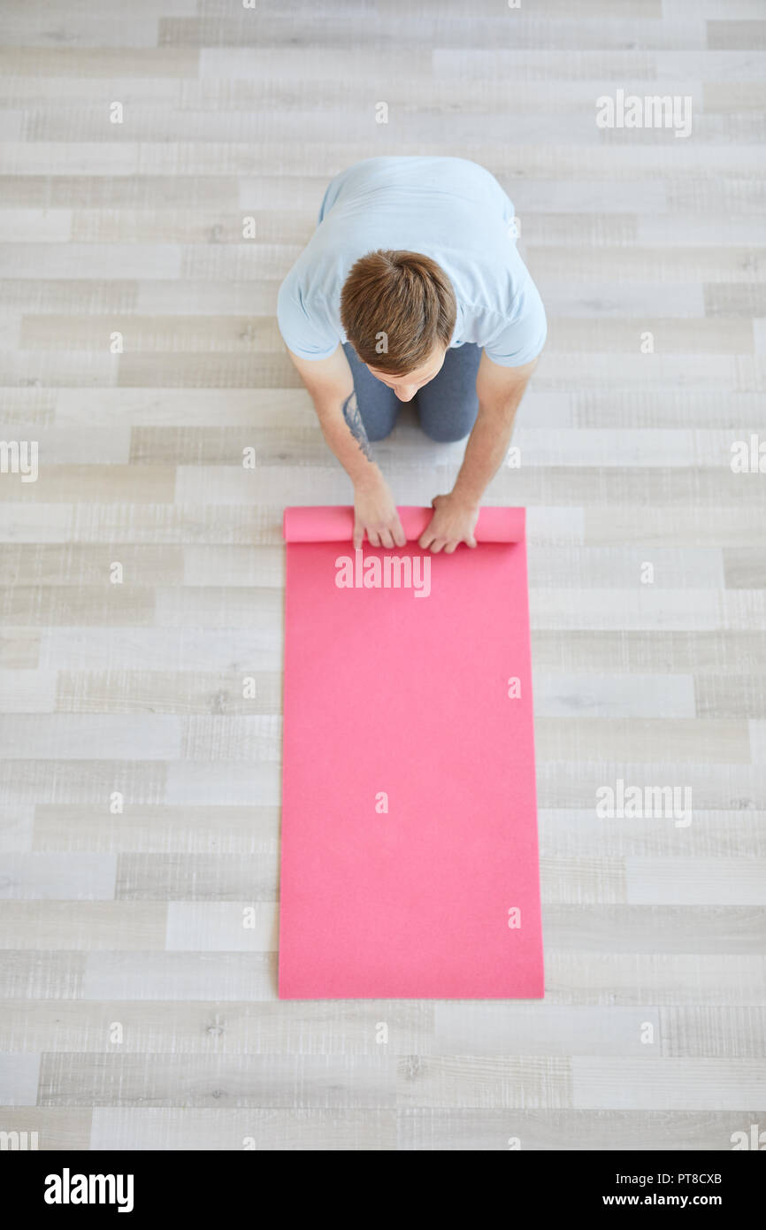 Young Sportsman Folding Pink Mat After Yoga Exercises On The Floor