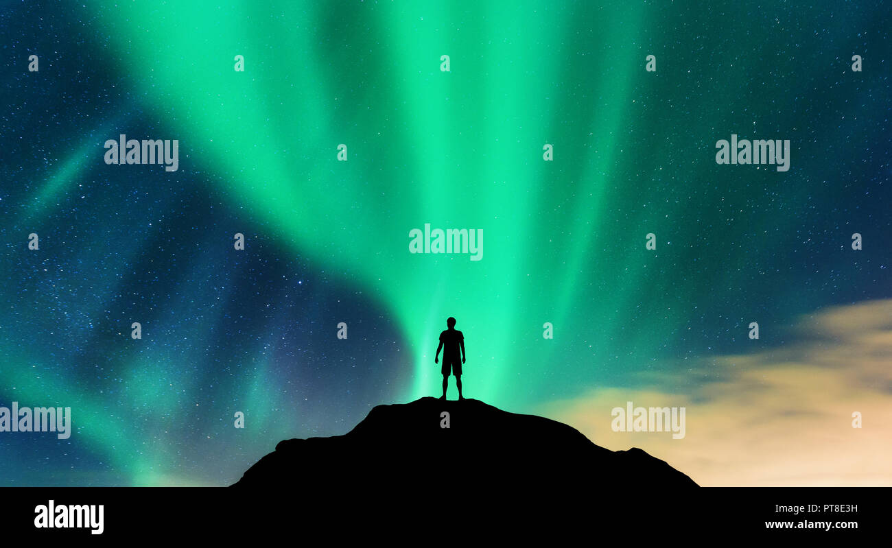 Aurora and silhouette of alone standing man on the mountain peak. Lofoten islands, Norway. Aurora borealis and young man. Sky with stars and green pol Stock Photo