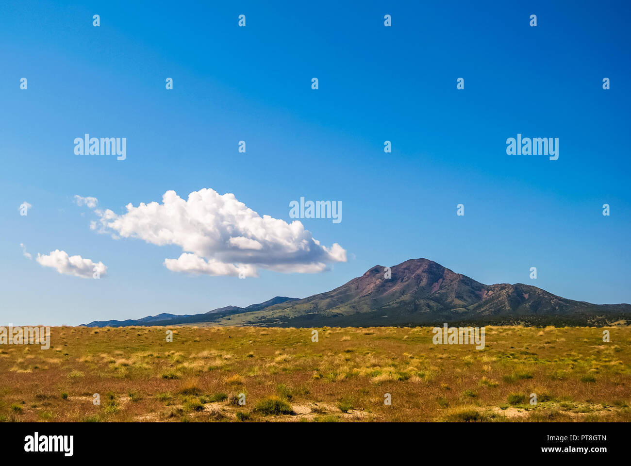 In the desert of western Utah, this small peak rises sharply from the vast fields of sage and grasses in the arid landscape. Above, a small cloud form Stock Photo