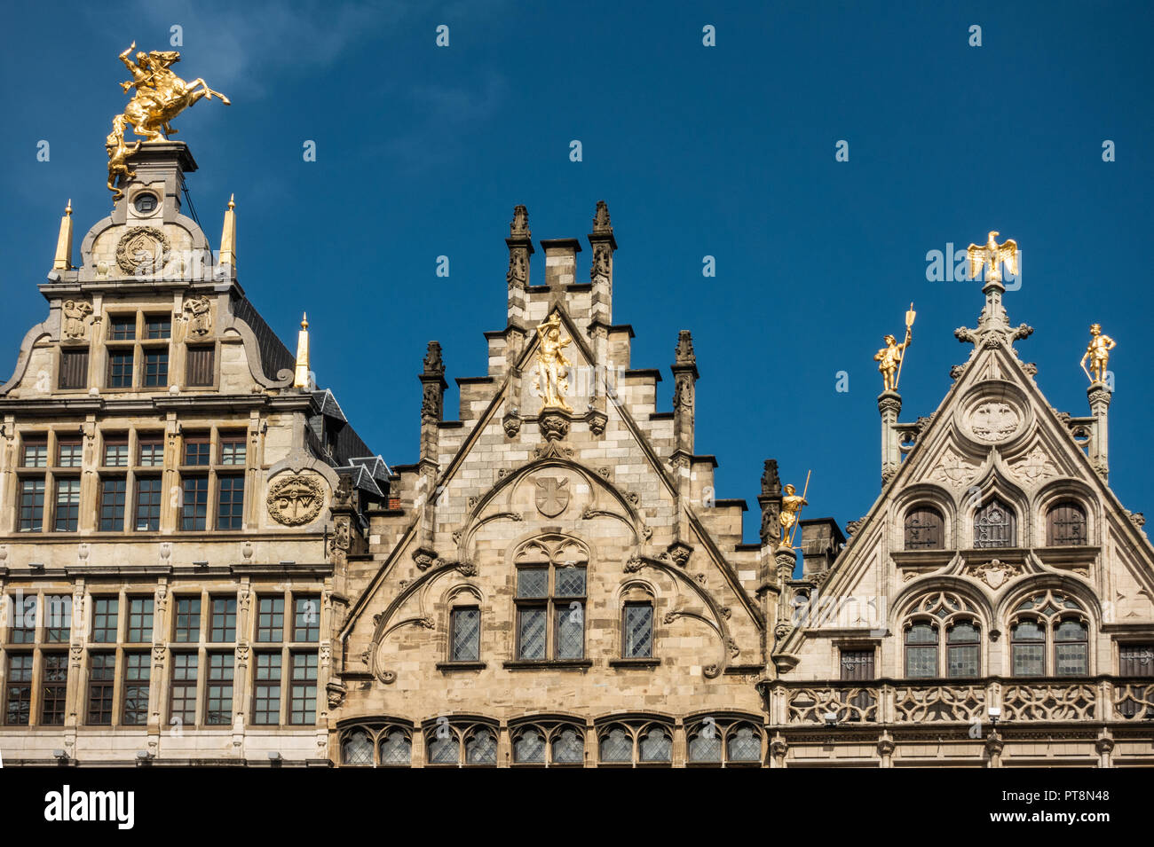 Antwerp, Belgium - September 24, 2018: Golden statues on top of the facades of guild houses on Grote Markt. Brown stones, arches under blue sky. Stock Photo