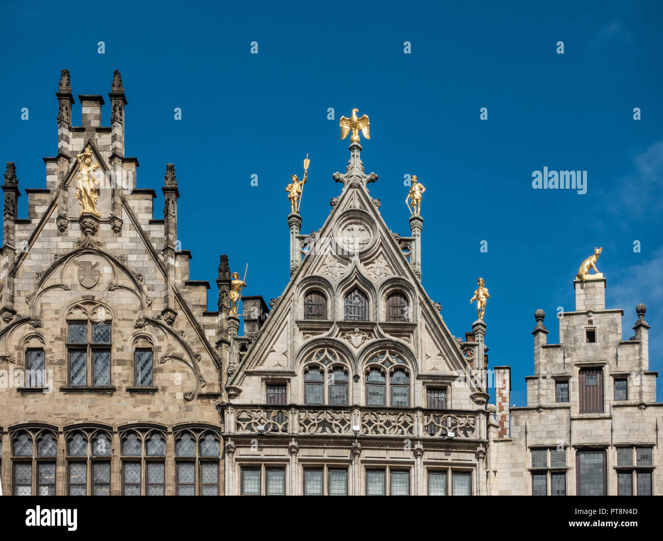 Antwerp, Belgium - September 24, 2018: Golden statues on top of the facades of guild houses on Grote Markt. Brown stones, arches under blue sky. Stock Photo