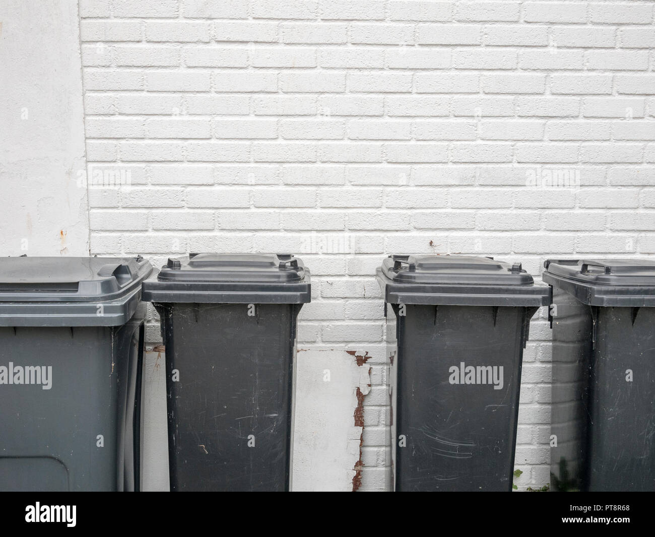 Four black wheeliebins against a white wall. Rubbish bin outside house. Redundant data metaphor. Stock Photo