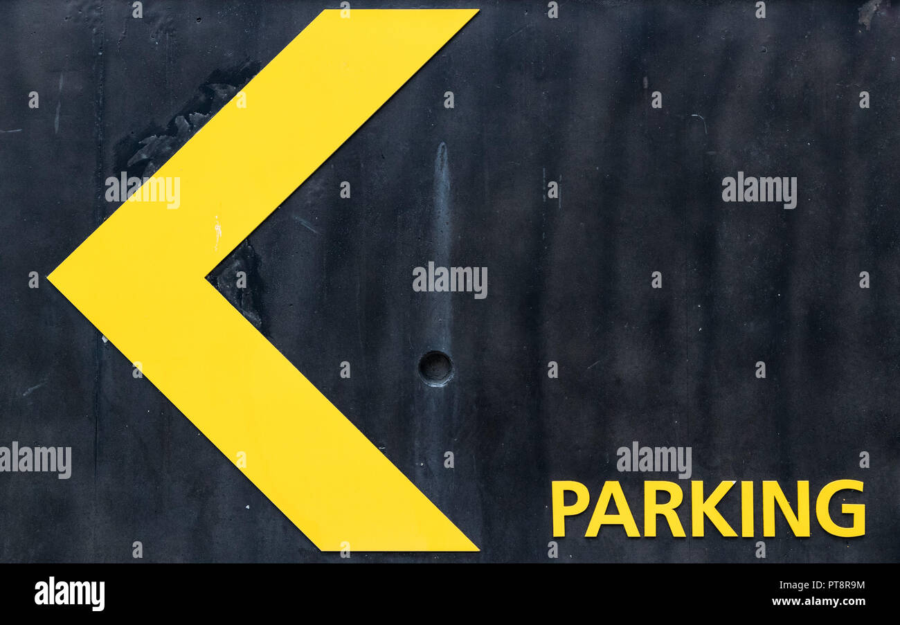 Parking direction sign in yellow on black grungy wall background Stock ...