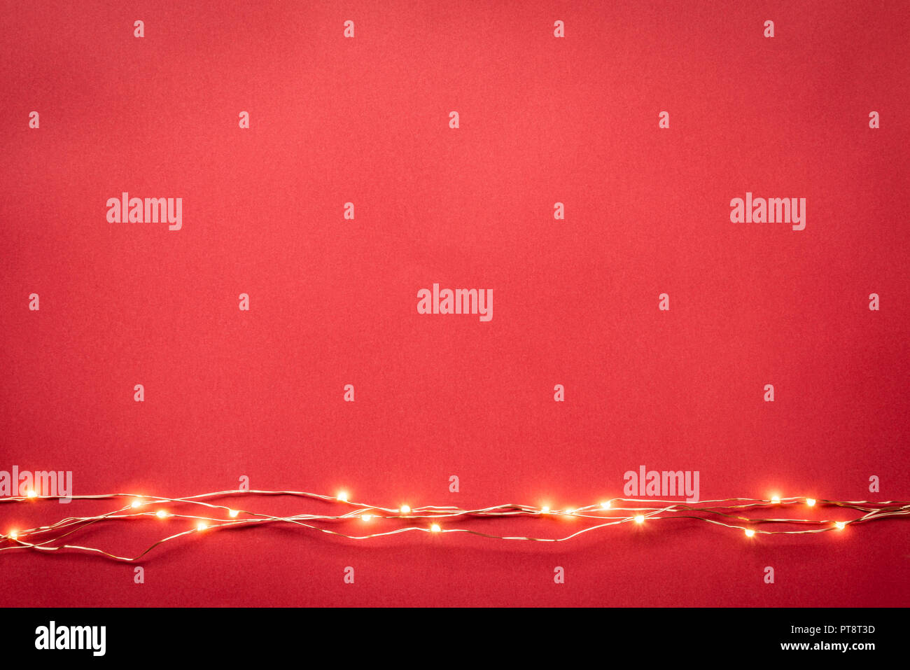 Christmas lights garland border over red background. Flat lay, copy space. Stock Photo