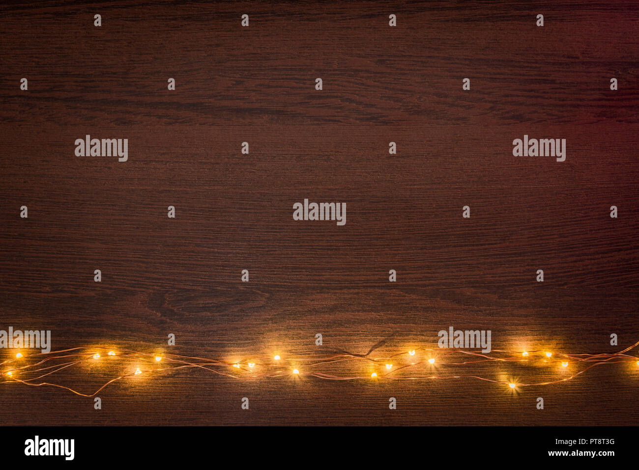 Christmas lights garland border over dark wooden background. Flat lay, copy space. Stock Photo