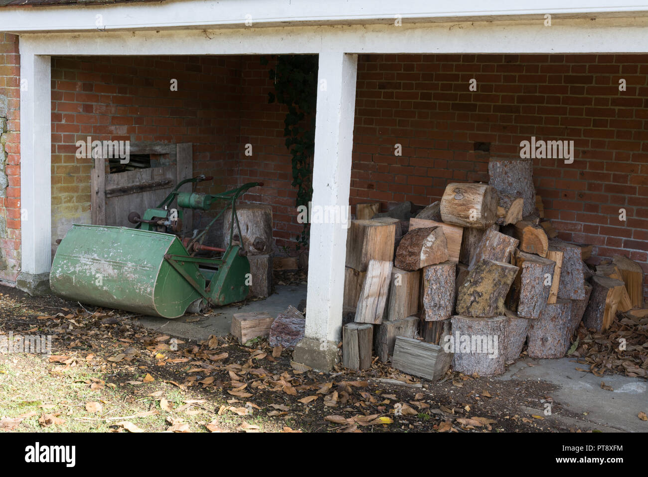 Outhouse (outbuilding, out-building) used for storage of logs and an old lawnmower (lawn mower) Stock Photo
