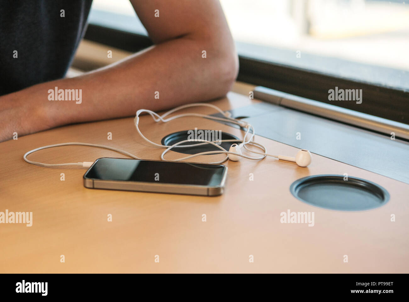Close-up of headphones and cell phone lying next to a man on the table in the train during the trip. Stock Photo