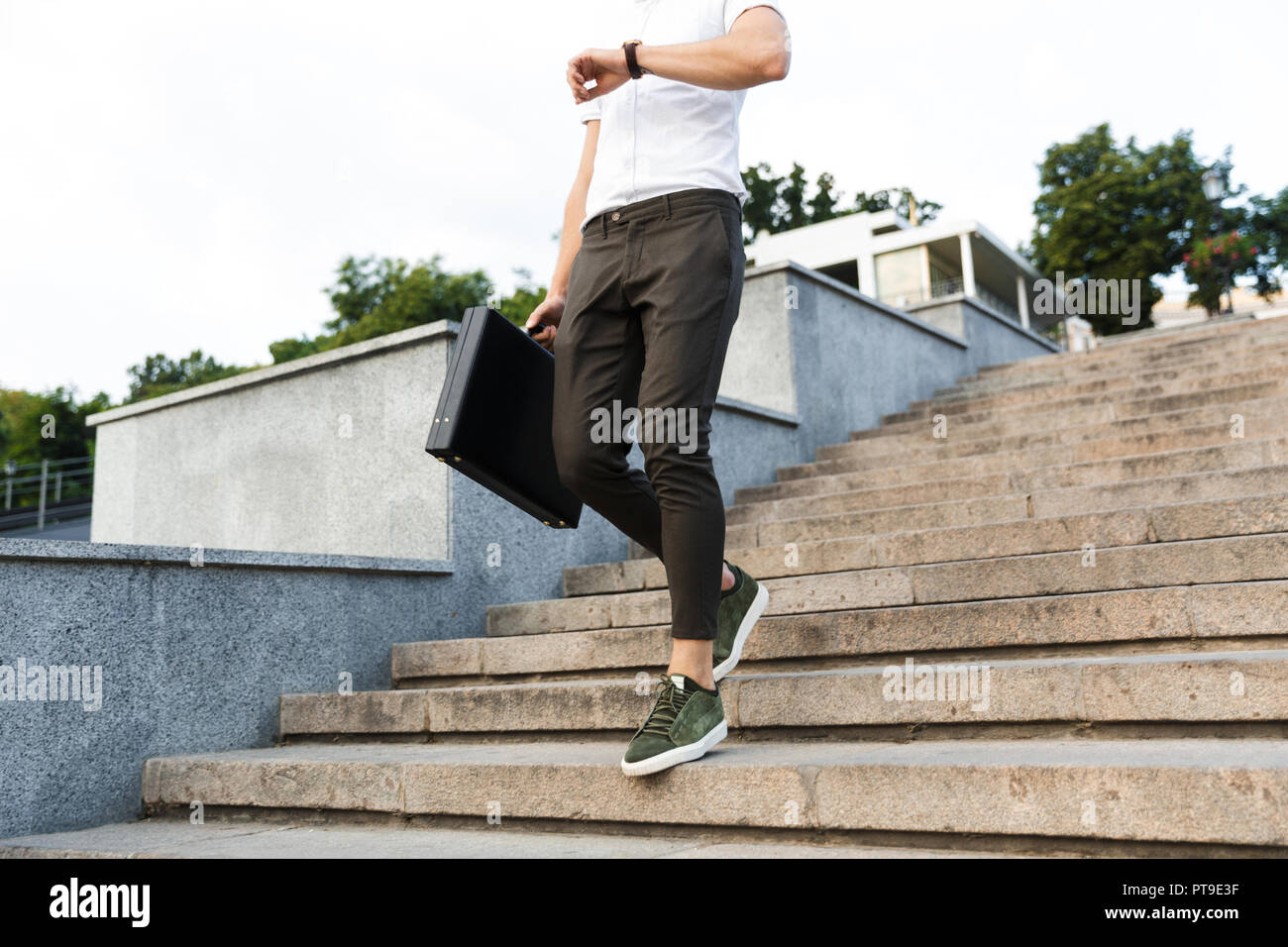 Cropped image of business man with briefcase looking at wrsistwatch while walking on stairs outdoors Stock Photo