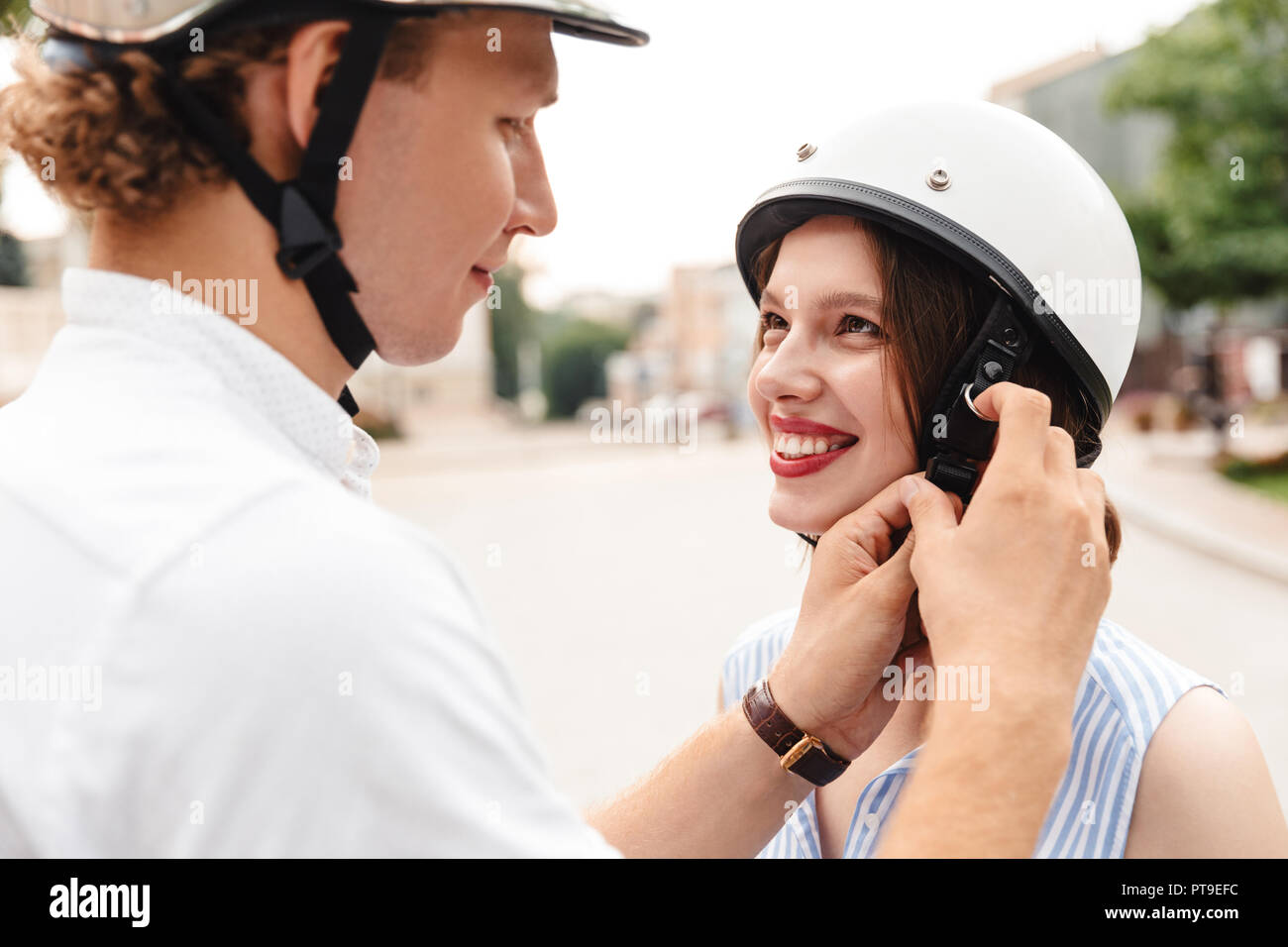 Cropped view of happy man fastens a helmet to his girlfriend outdoors Stock Photo