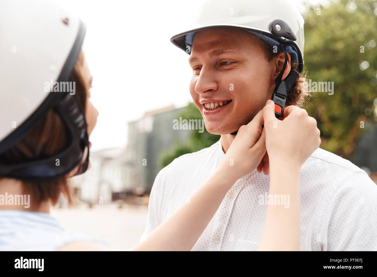 Cropped view of happy woman fastens a helmet to her boyfriend outdoors Stock Photo