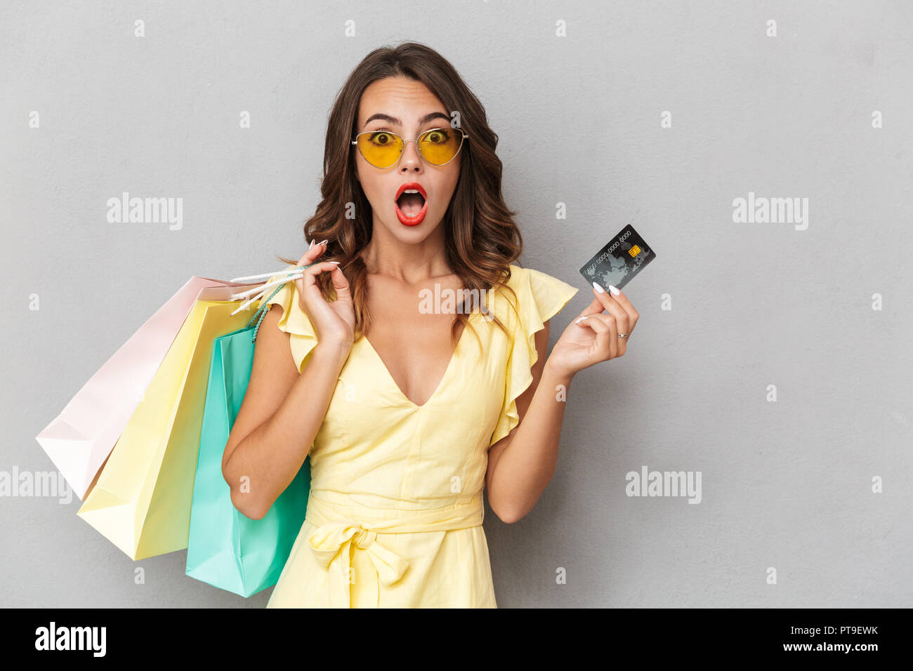 Portrait of a shocked young girl in dress standing over gray background ...